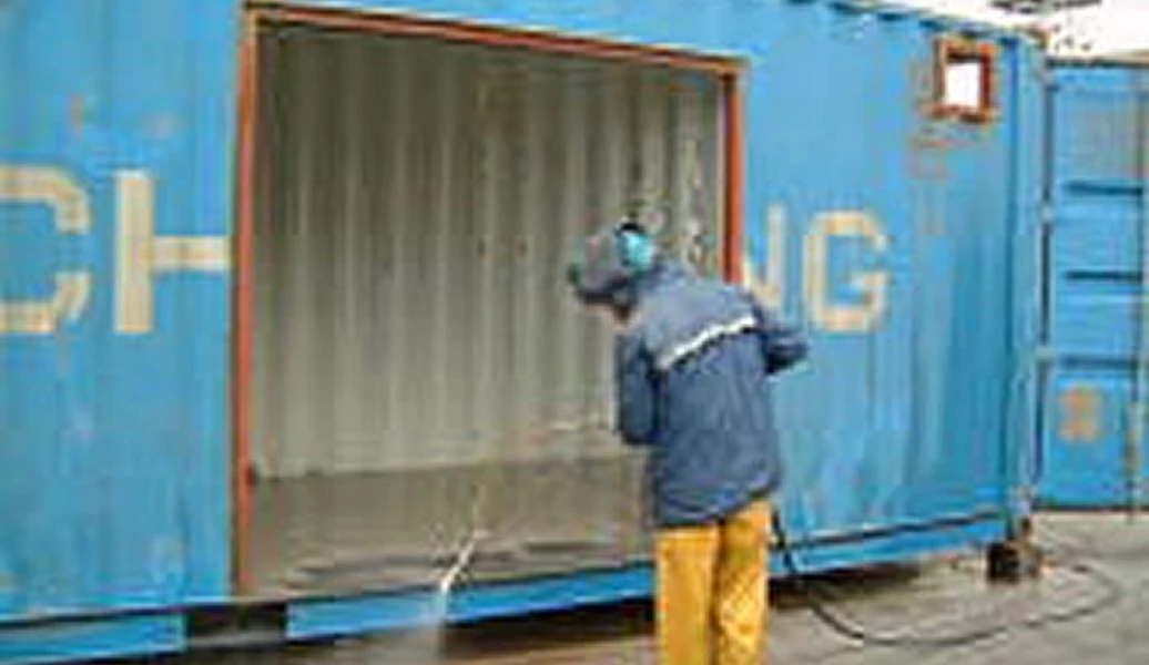 防護マスクを着けた作業員が金属面にサンドブラスト処理を施している様子